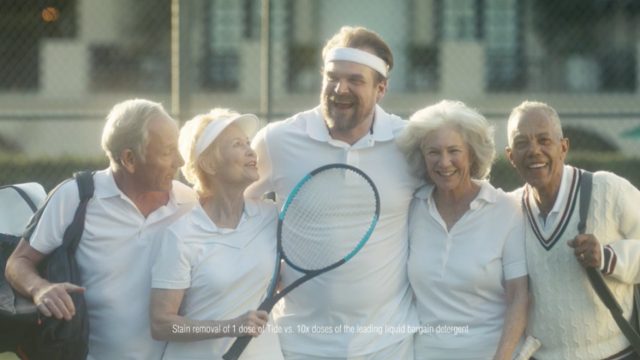 David Harbour hugs group of older people playing tennis in white shirts for Tide ad.