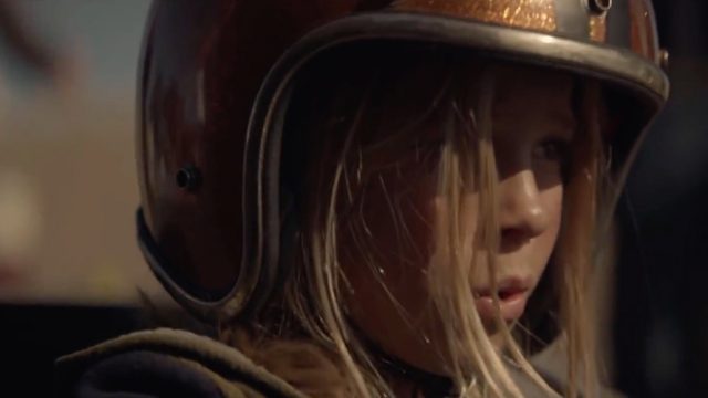 A blonde girl is wearing a helmet as she looks off into the distance; the image is taken from an Audi advertisement