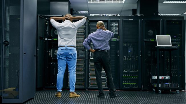 two men looking at computer servers with their backs turned looking frustrated or confused