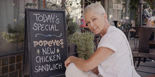 Kim Sanchez, Sweet Dixie Kitchen owner, crouches by a sign that says 