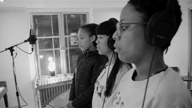 Black and white photo of three young people singing in a music studio with white walls