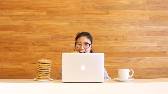 Connie Chweh sits behind an Apple laptop, with a stack of cookies and a mug.