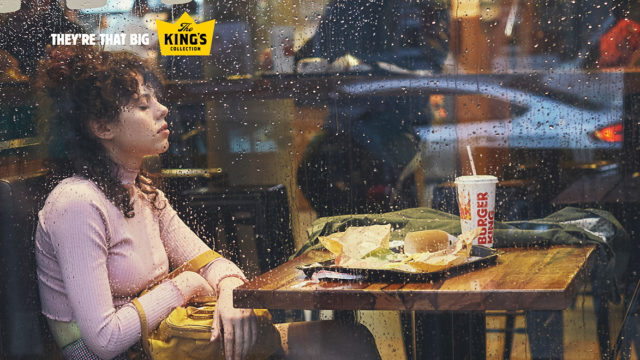 Rain splatters a window as a Burger King customer falls asleep sitting in her booth.