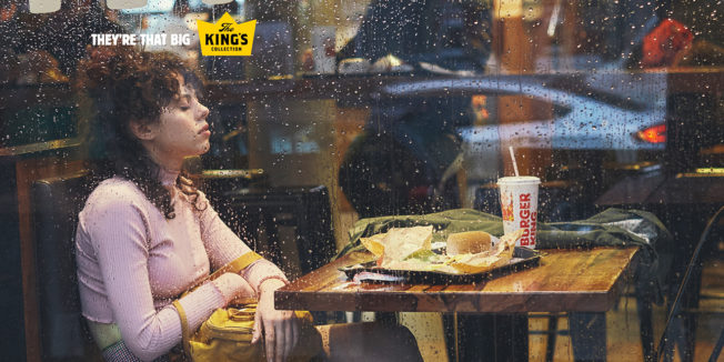 Rain splatters a window as a Burger King customer falls asleep sitting in her booth.