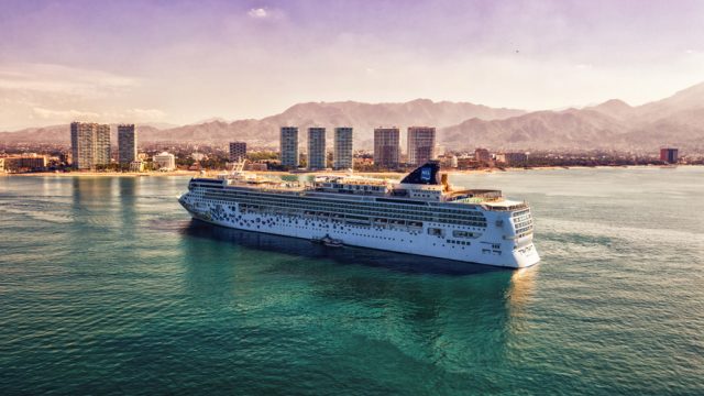 image of a cruise ship with mountains and buildings in the background