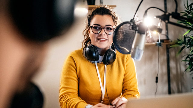 a young woman records a podcast into a microphone