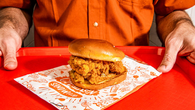 a popeyes employee holding a tray with the popeyes chicken sandwich on it