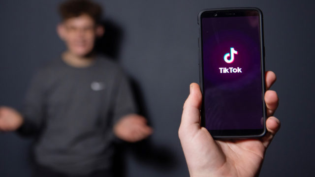 blurred person shrugging in the background and phone in hand showing tiktok logo in foreground