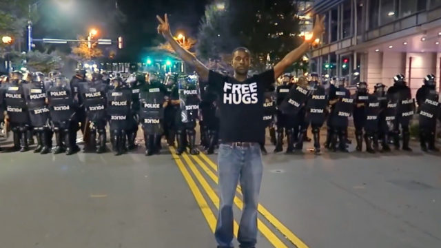 Man standing in front of a police blockade holding the peace signs with a 