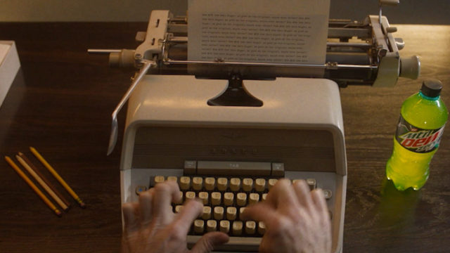 Hands typing on a typewriter; mountain dew bottle on the right side
