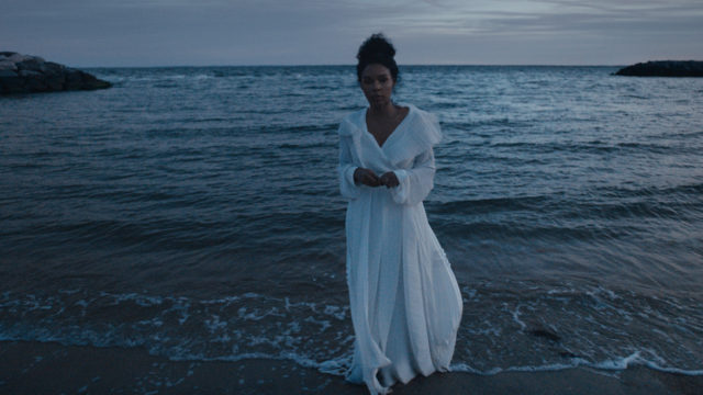 janelle monae standing on a beach in a white dress