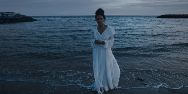 janelle monae standing on a beach in a white dress
