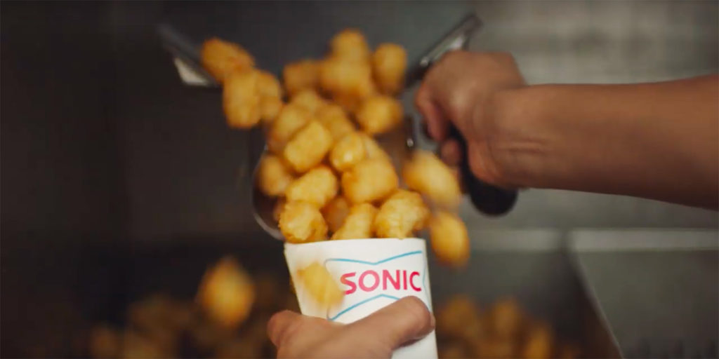 A hand holding Sonic tater tots pushing the tater tots on to a tray