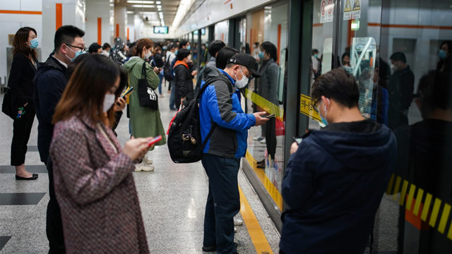 people standing on a subway platform with masks on using their phones