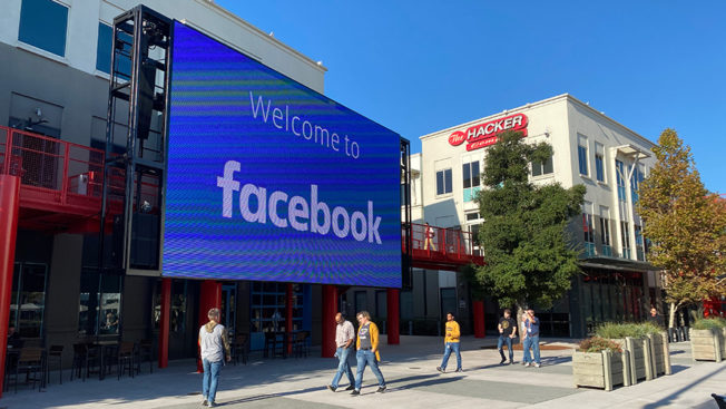 a facebook billboard on the street with people walking past it