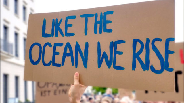 a cardboard sign that says like the ocean we rise