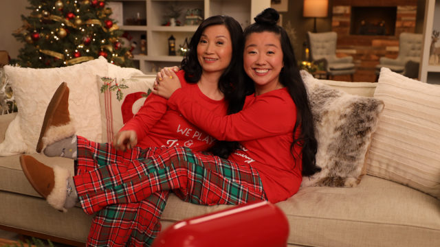an asian mom and her daughter sitting on a couch dressed in red and hugging