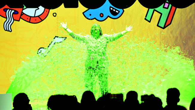 a person covered in green slime with their arms wide open on a stage