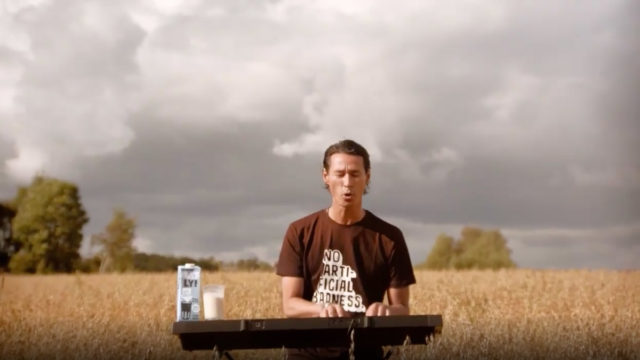 a man sitting in a field on a cloudy day drinking oatly oat milk