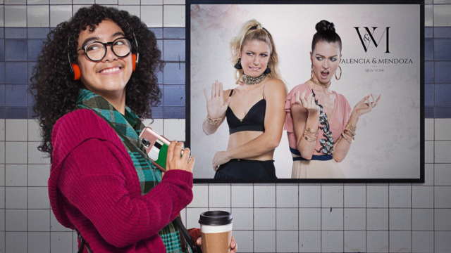 a girl with curly hair, glasses and headphones on in front of a poster