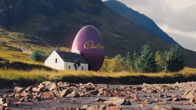 a giant purple cadbury egg next to a small house nestled next to a mountain