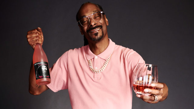 a photo of snoop dogg posing with a glass and bottle of his new brand of wine Snoop Cali Rosé