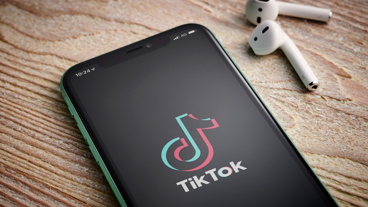 a photo of a phone on a table showing tiktok app open with airpods next to it