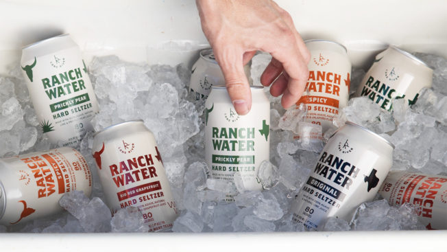 A hand reaches into a cooler full of ice and cans of Lone River Ranch Water