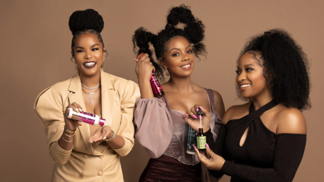 three black women smiling holding hair care products
