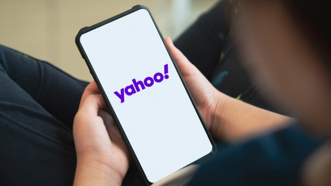 person holding a cellphone the screen of which says yahoo! on a white background