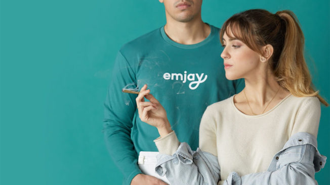 In a promotional image for cannabis delivery service Emjay, a woman holds a lit joint while standing next to a man in an Emjay long-sleeve shirt