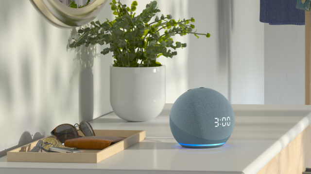 A smart speaker sits on an entryway table with sunglasses and a plant.