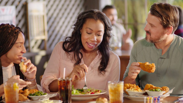 an interracial family eating fried chicken and southern food together in a restaurant