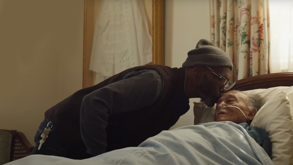 A man gently kisses an elderly man in a hospital bed on the forehead