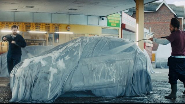 Men wash a car despite it being covered by a sheet