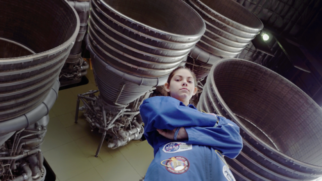 A young girl standing in front of rocket jets with her arms crossed