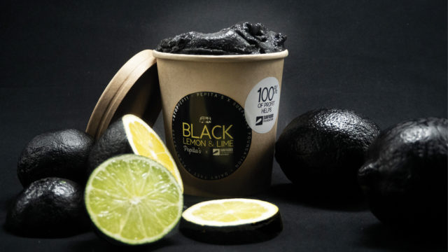 A pint of black ice cream sits next to lemons and limes whose rinds are painted black