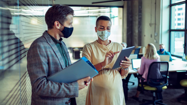 Two people in an office space wearing masks and talking