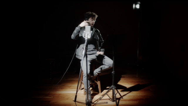 A man sits in a spotlight in front of a microphone