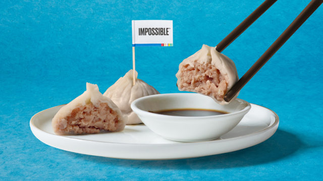 Asian dumplings made with Impossible plant-based pork are shown on a plate with chopsticks holding one dumpling