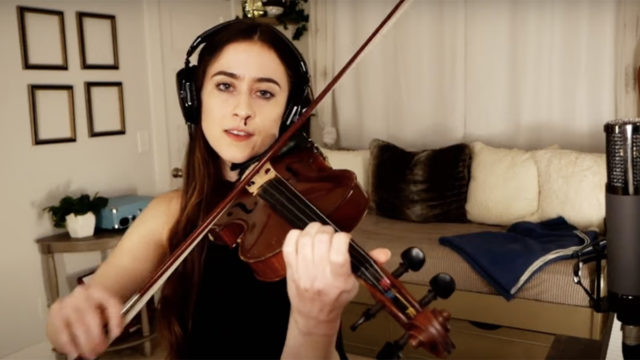 A woman plays violin while blood drips down from one nostril