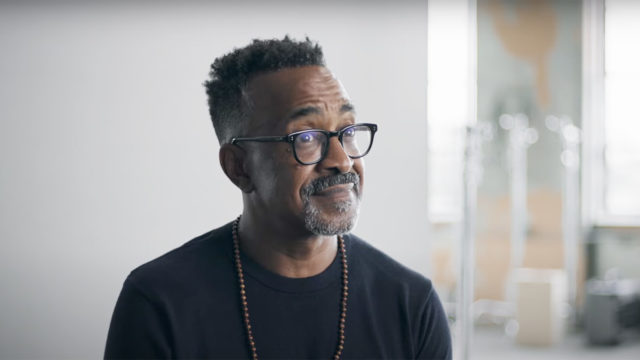 Actor Tim Meadows wears glasses and a long bead necklace while looking with surprise