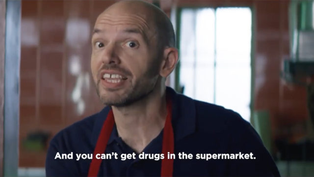 Paul Scheer wears a grocer's smock while talking to customers at a store