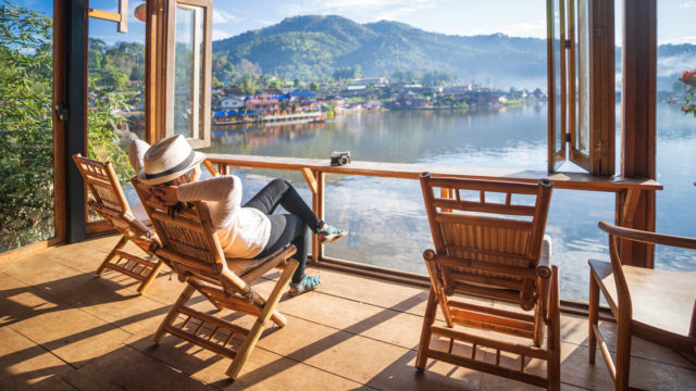A man sits in a chair on a deck overlooking a lake
