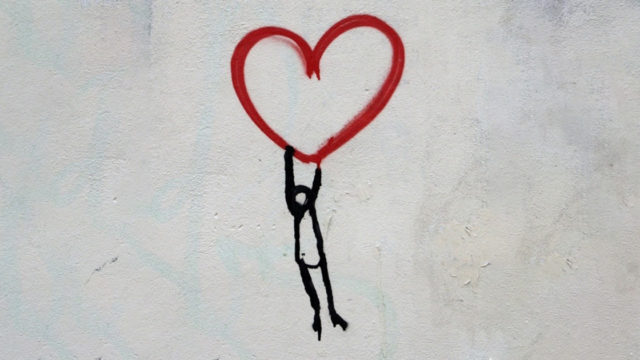 Street art of man holding on to a red heart.