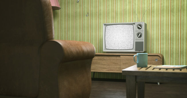 Photo of an empty armchair facing an old tv with static.