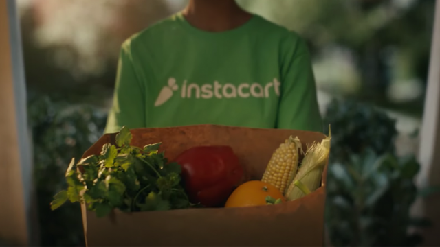 someone holding a box of vegetables with a green instacart shirt on