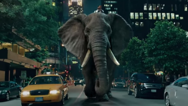 A man rides an elephant down a city street.